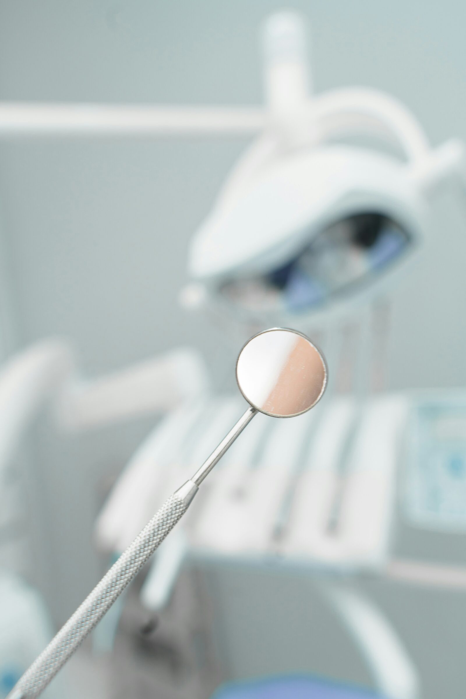 Dental mirror reflects skin and light in a blurred dentist's office.