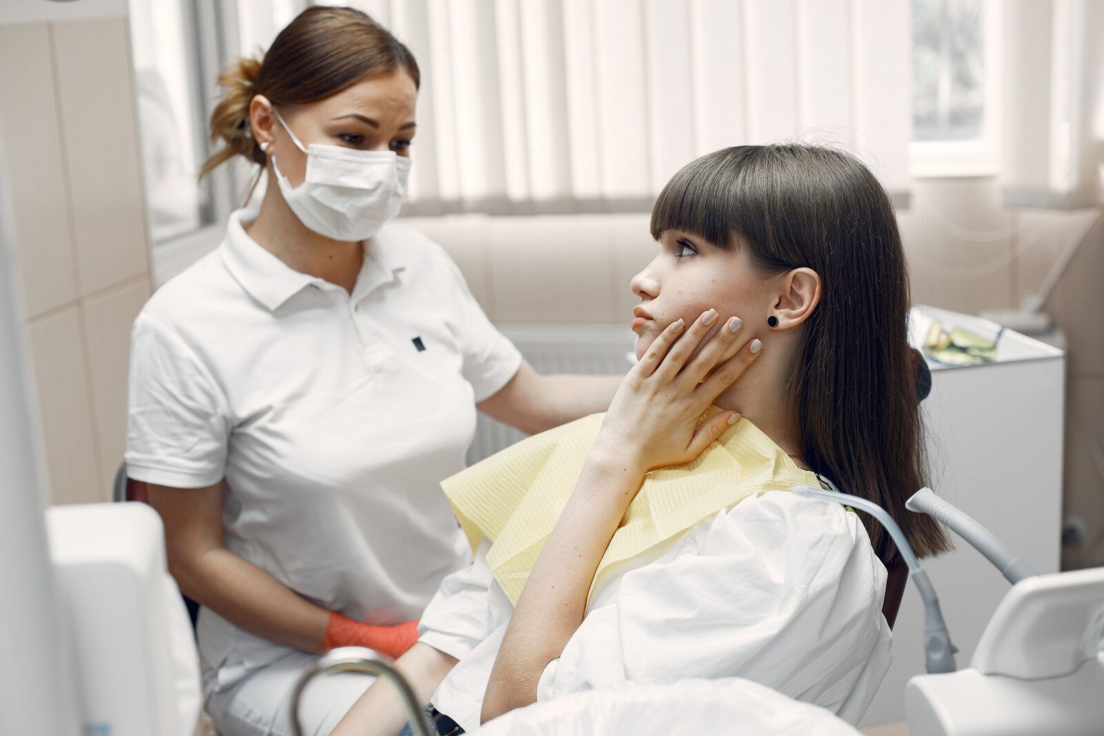 Dentist comforts patient holding jaw in a dental chair.