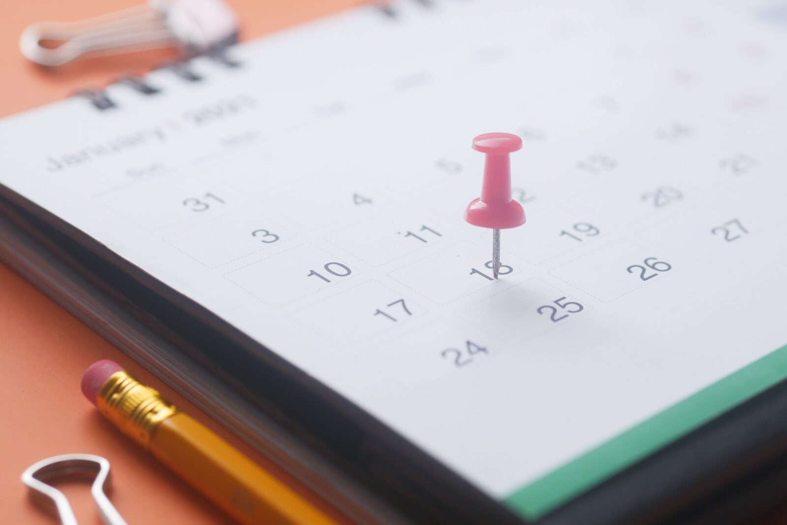 Pink pushpin marking the 18th on a desk calendar.