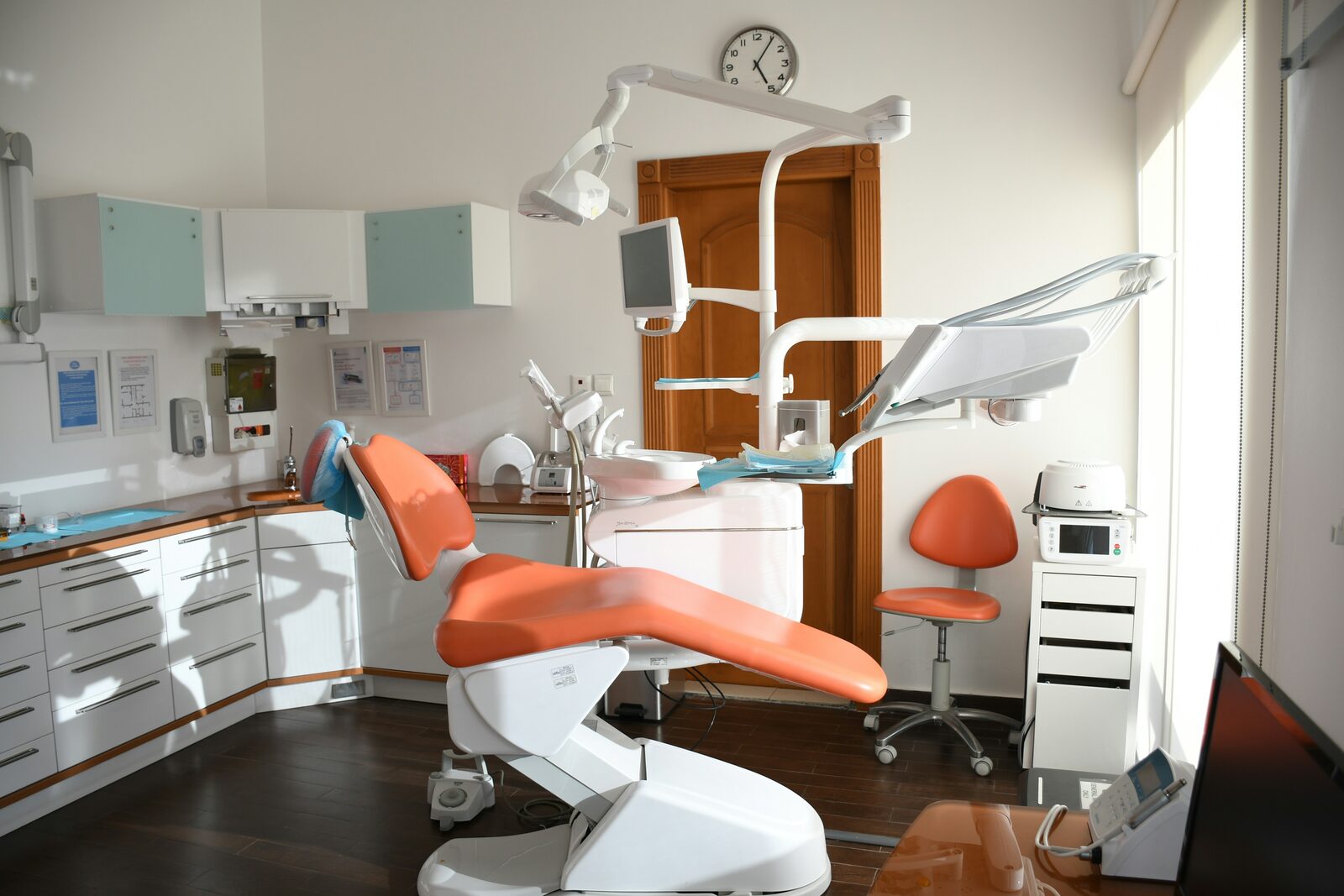 Empty, modern dental office with an orange patient chair and equipment.